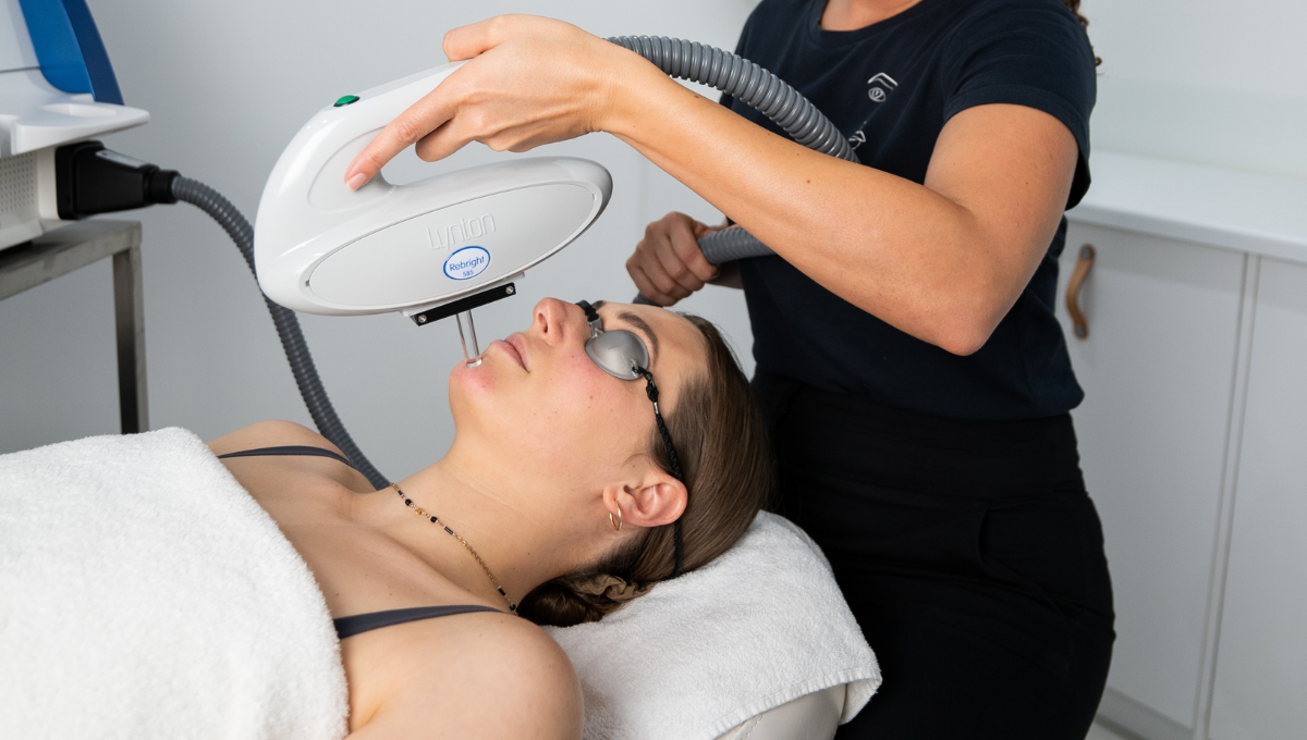A Dermal Therapist performing an IPL test patch on a female client who is laying down on a treatment bed