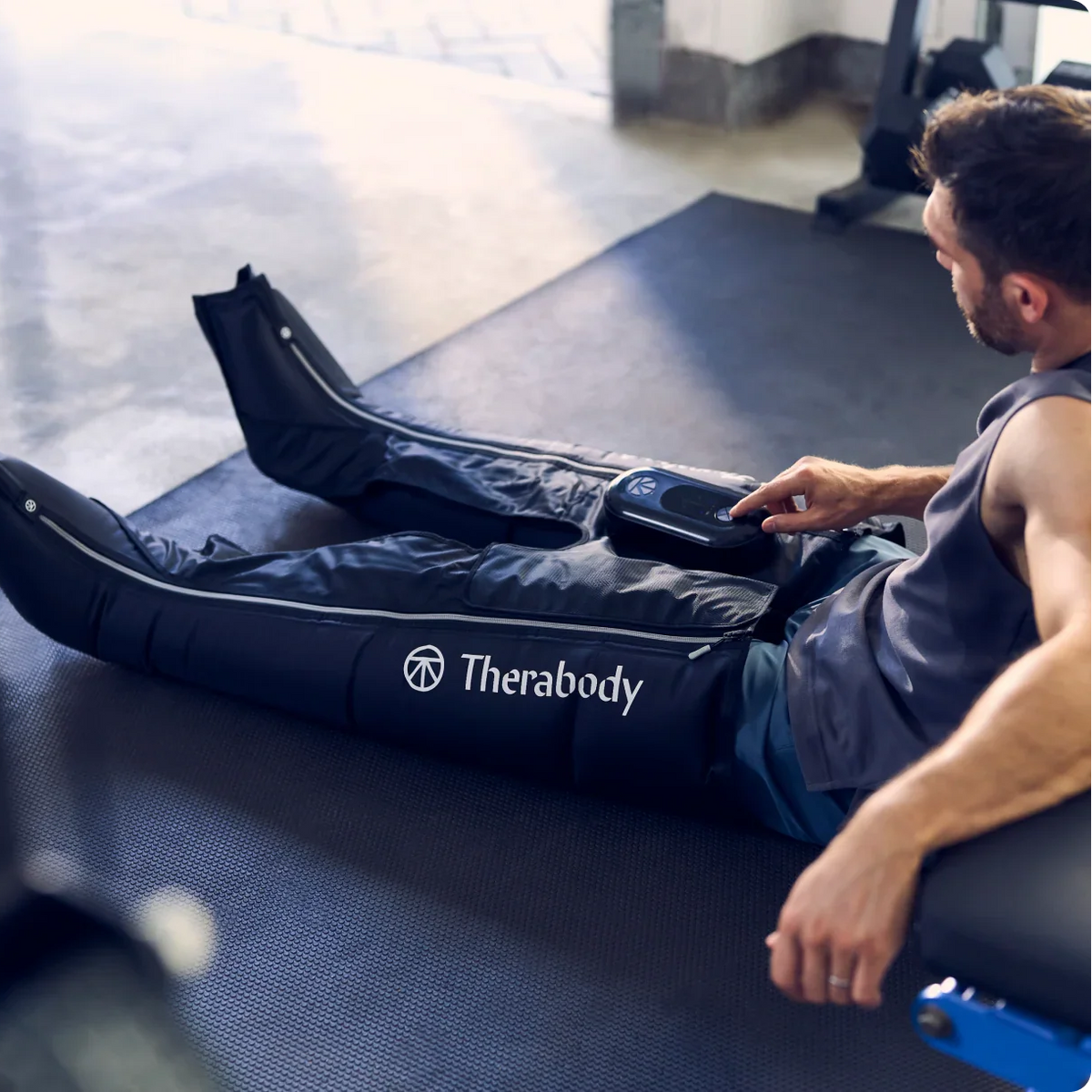 Person using a Therabody leg compression device in a gym setting