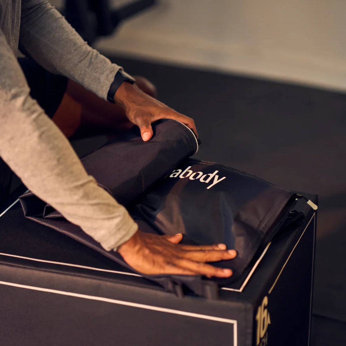 Person unrolling a mat with 'abody' branding from a box.